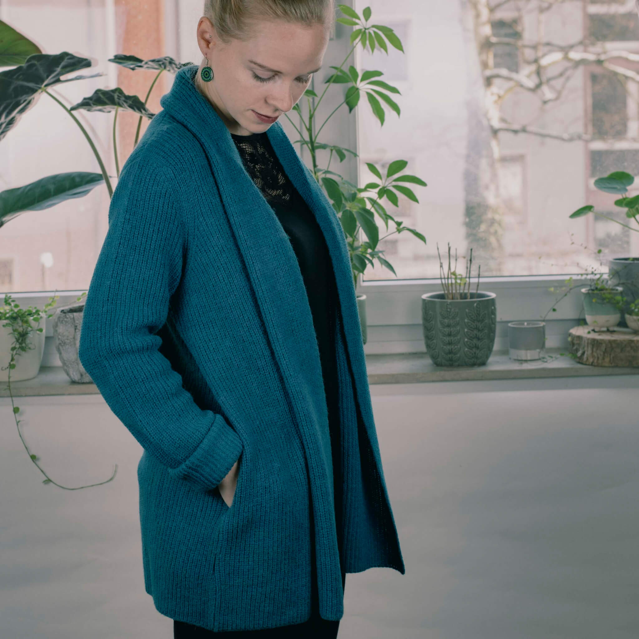 Weibliches, blondes Model trägt die Mira Alpaka Strickjacke von Alpakin in dunkeltürkis