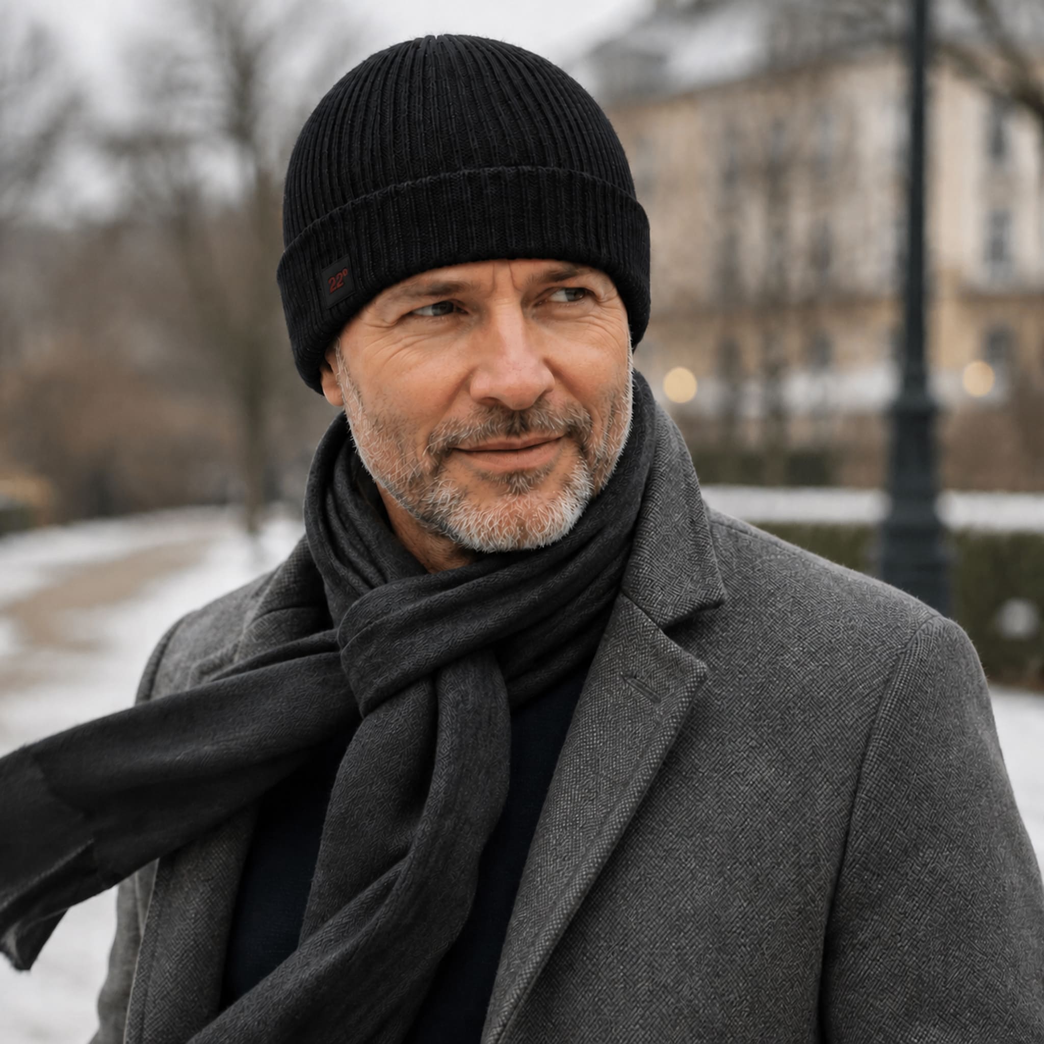 Mann mit grauem Bart trägt die Winddichte Alpaka Beanie Mütze in schwarz zu Mantel an kaltem Wintertag mit Wind
