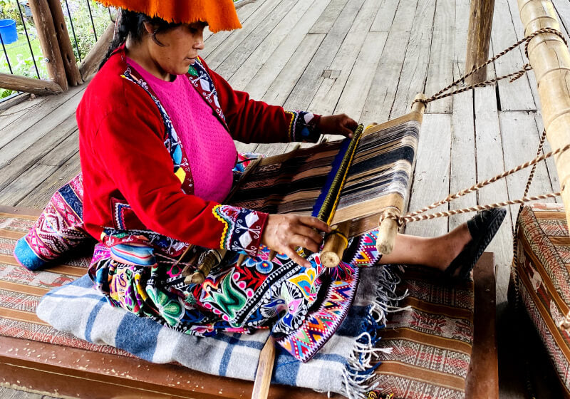 Peruanerin in typisch-bunter Kleidung webt mit Alpakawolle