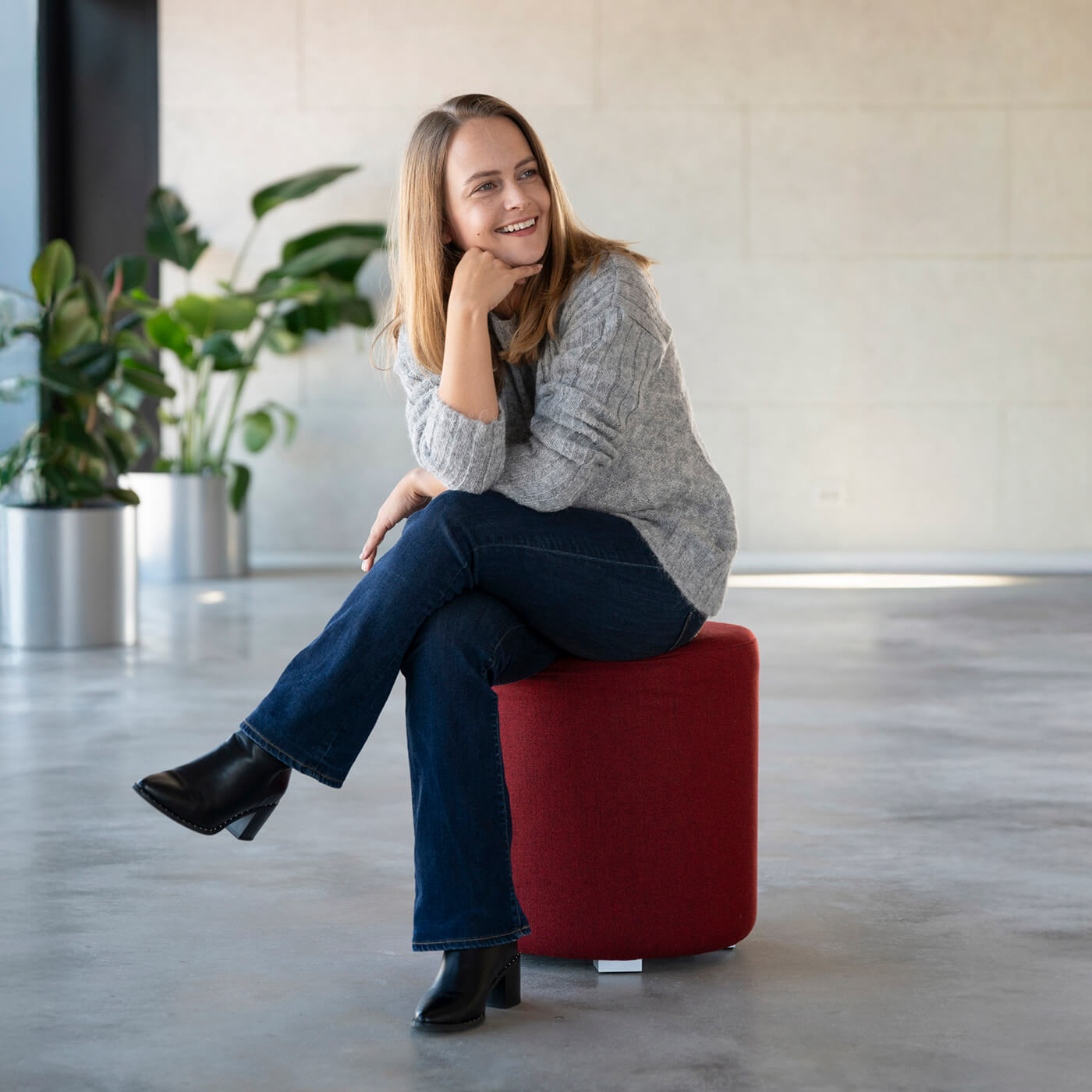 Model sitzt mit ihrem grauen Andes Alpaka Wollpullover auf einem roten Hocker