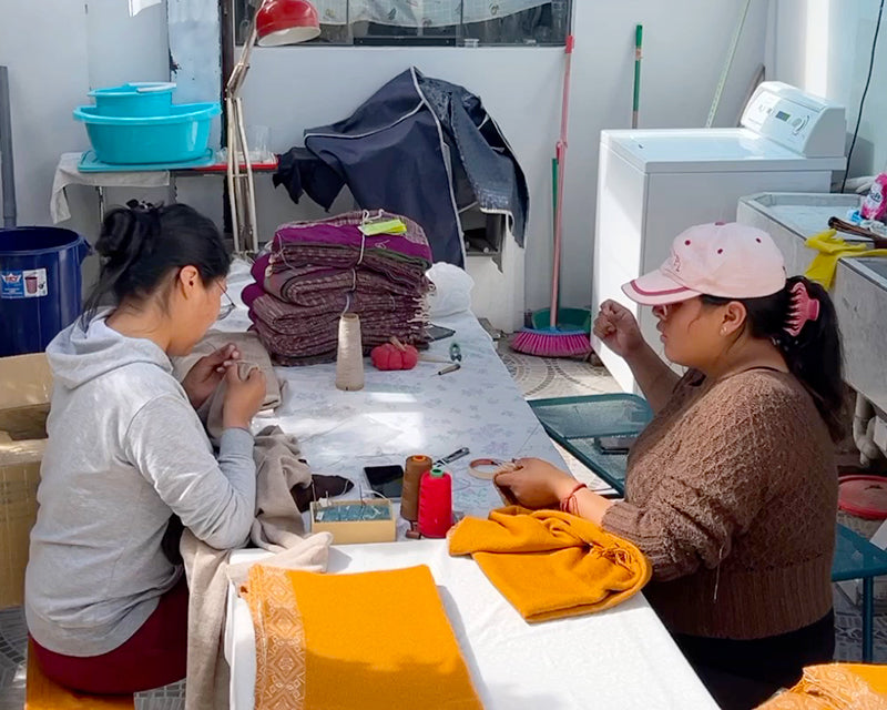 Fertigung Alpaka Poncho FLOR von Frauen in Peru, die am Tisch sitzen und arbeiten