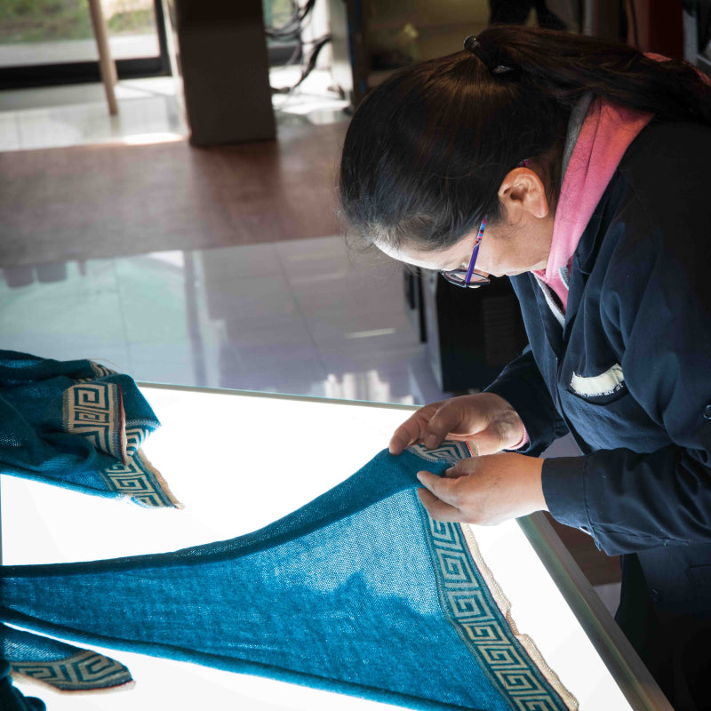 Peruanische Schneiderin prüft den Alpaka Poncho Luz für Damen unter Licht auf mögliche Fehler im Textil