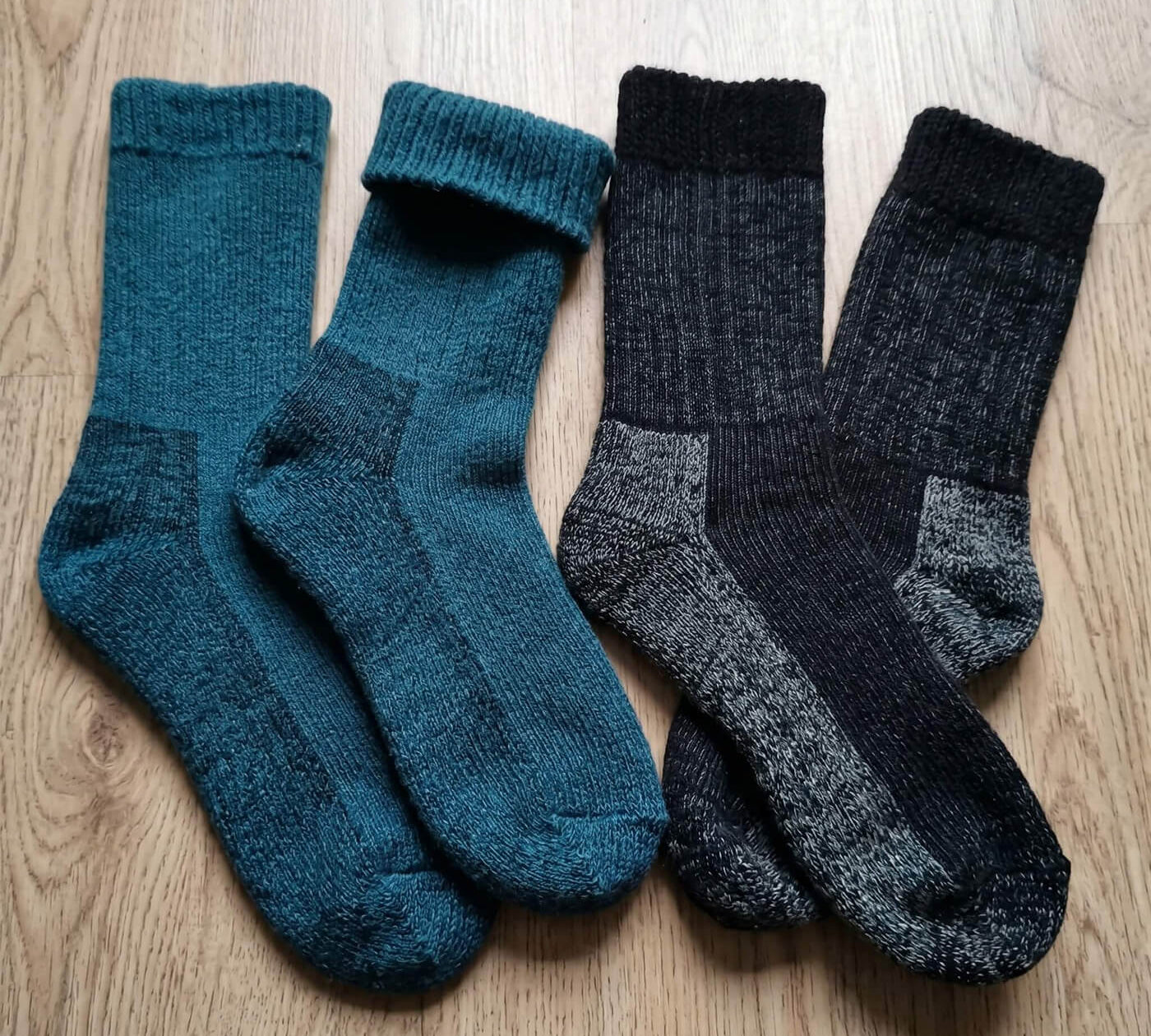 Wärmste Alpaka Thermosocken in schwarz und dunkeltürkis auf Holzboden gelegt