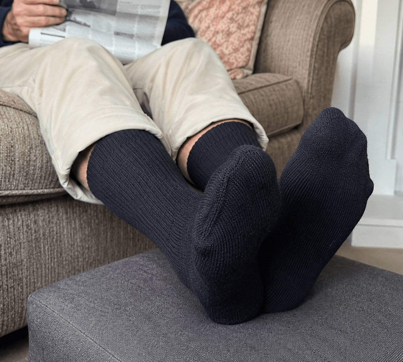Mann sitzt komfortabel mit seinen Diabetikersocken auf dem Sofa und liest Zeitung