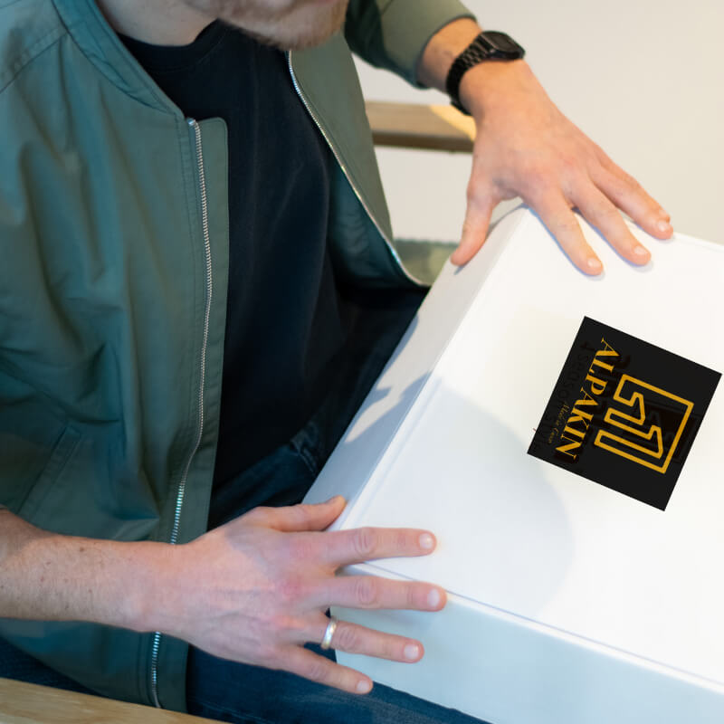 Weißer Alpakin Karton mit Logo verschlossen in den Händen eines Mannes