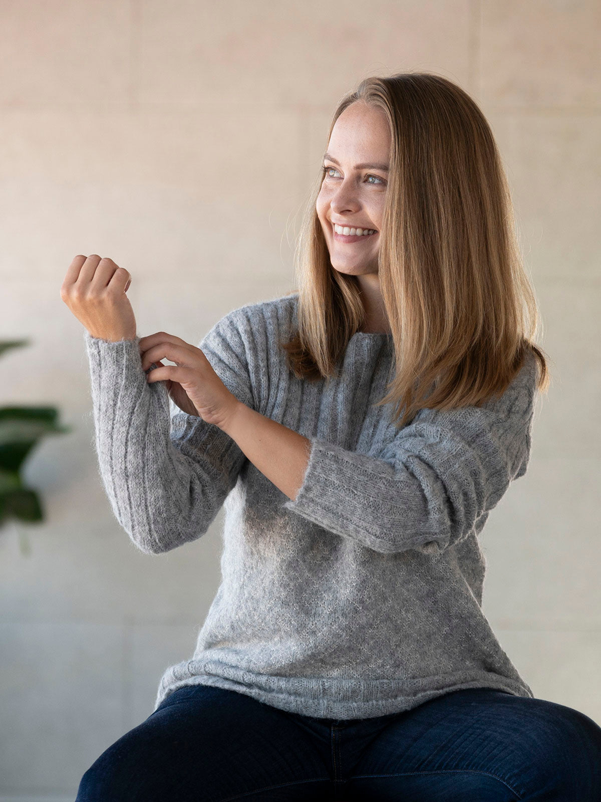 Frau fühlt das weiche Textil des Andes Alpaka Wollpullovers in Naturfarbe hellgrau und lächelt - Mobile Version