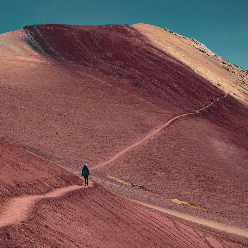 Frau in bunter Landschaft in Peru, die auf einem weitläufigen Weg wandert