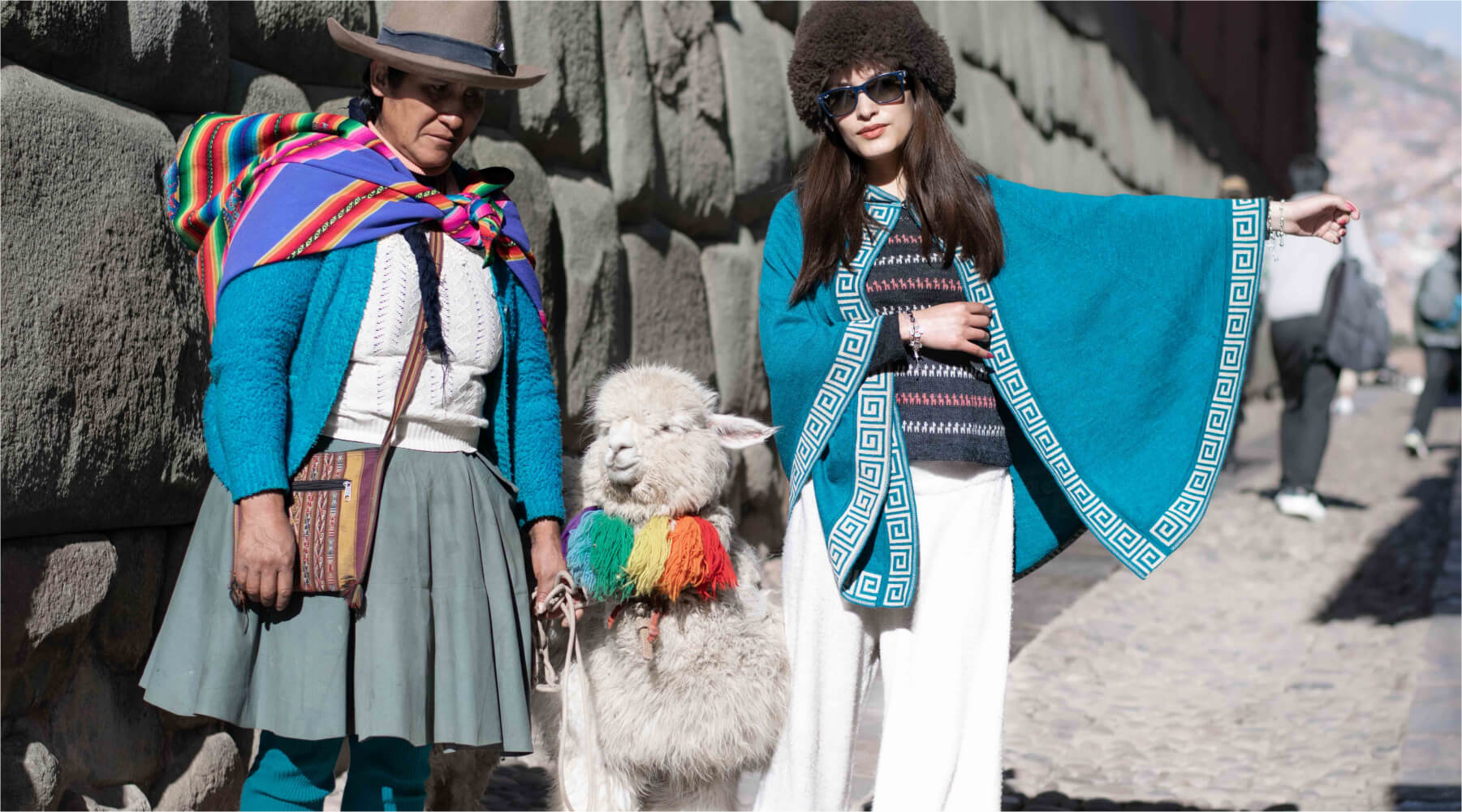 Model mit Peruanerin und Alpaka an ihrer Seite trägt LUZ Alpaka Poncho in Cusco, Peru