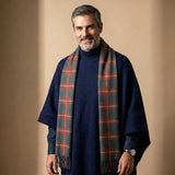 Ein attraktiver 45-järiger Mann mit Bart und grauen Haaren trägt den Herren Poncho mit Kragen British-Style - in Kombination mit dunkelrotem Schottenkaro Schal